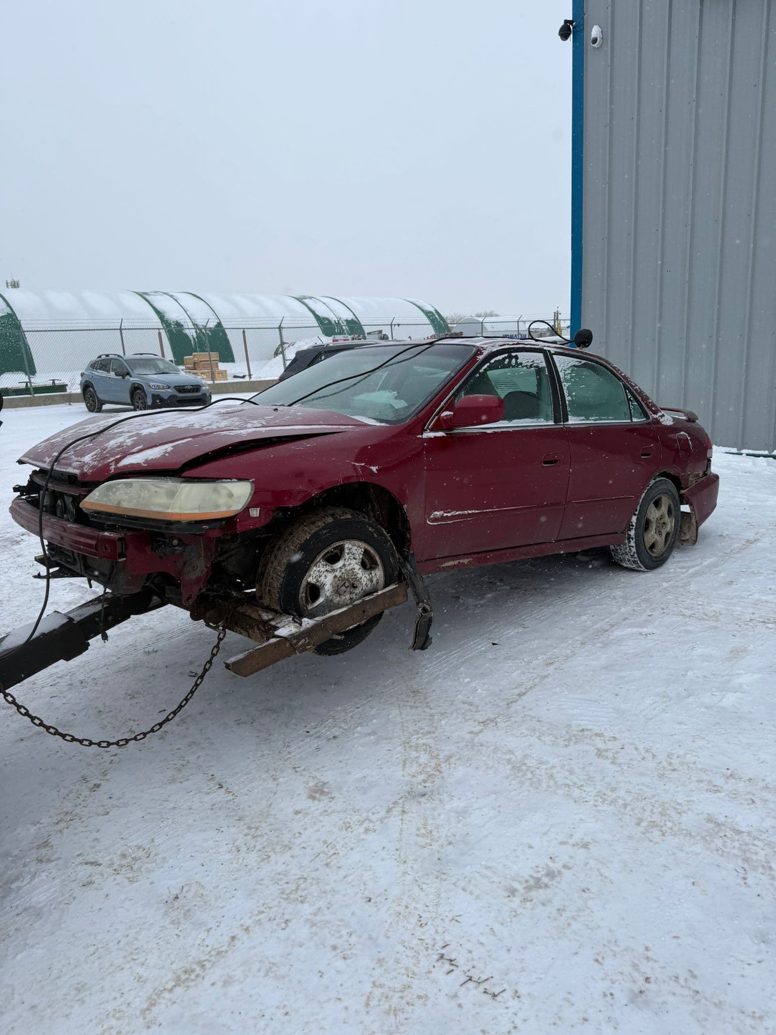Damaged red sedan ready to be sold as a junk car for cash in snowy Edmonton